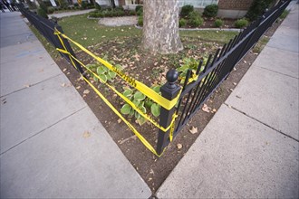 Yellow caution tape taking the place of a missing section in a metal fence