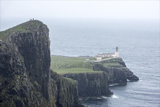 Walkers on clifftop watching Neist Point Lighthouse in the mist on the Isle of Skye