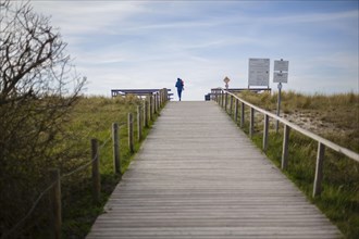 A woman with a child in her arms walks across a beach access on the Fischland-Darss-Zingst peninsula in Mecklenburg-Western Pomerania. Arenshoop