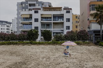 A woman sits in front of a house on the beach of Durres
