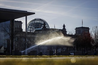 A water sprinkler waters a meadow in front of the Reichstag in the morning. Berlin
