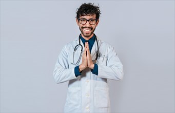 Young doctor with palms together. Smiling doctor putting palms together on isolated background. Handsome doctor with hands together isolated