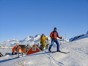 Ski mountaineers in front of colourful wooden houses in Tasiilaq in winter