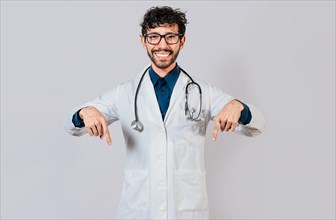 Young doctor pointing a promotion down. Handsome doctor pointing down an isolated advertising space. Happy doctor pointing fingers down