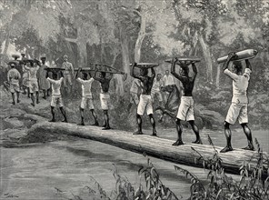 Nigerian porters carrying gun parts across a river to fight slavery