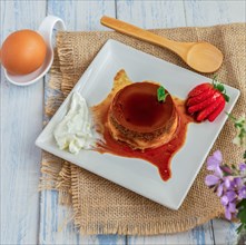 Egg custard with cream and strawberries on a white plate on a blue wooden table with flowers