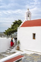 Young woman with red skirt at a Cycladic white and red Orthodox church