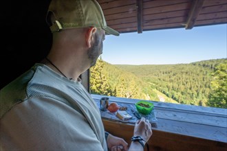 Man with cap takes a break and eats Vesper on the Fautsburg with view of the Black Forest