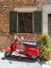 Red Vespa in front of the window of a typical stone house