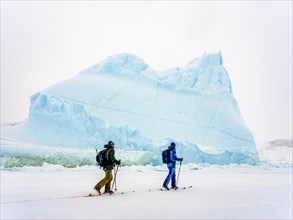 Ski tourers in front of iceberg in frozen Kong Oscar Fjord