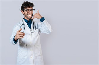 Young doctor making call gesture isolated. Smiling doctor making call gesture and pointing at the camera