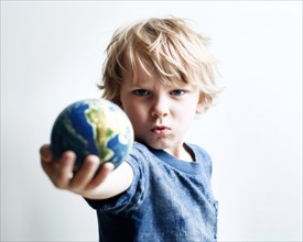 A five-year-old blond boy with an angry look demonstratively stretches out his arm with a globe in his hand