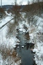 A small river in a regulated streambed and a wintry landscape. There are no walkers on the footpath along the water