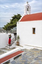 Young woman with red skirt photographed at a Cycladic white and red Orthodox church