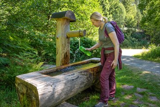 Hiking woman fills drinking bottle at the wooden fountain on the hiking trail Sprollenhaeuser Hut