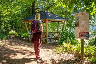 Hiker Woman Looking at board next to wooden pavilion in the forest