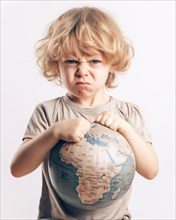A young boy with an angry look holds a globe in his hands
