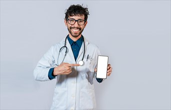 Smiling doctor holding and pointing at cell phone screen. Young doctor showing and pointing at smatphone screen isolated