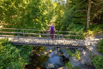 Woman standing on wooden bridge looking at the river on the hiking trail Sprollenhaeuser Hut