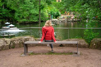 Woman sitting on bench in front of pond in spa gardens