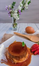 Egg custard with cream and strawberries on a white plate on a blue wooden table with flowers