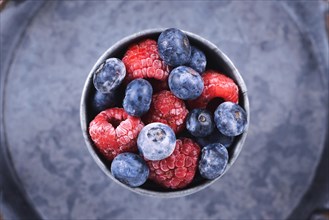 Top view of mixed blueberry and raspberry fruits in iron cup