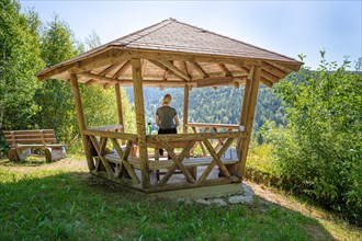 Woman eating pretzel in wooden pavilion and looking at the endless forest on the hiking trail Sprollenhaeuser Hut