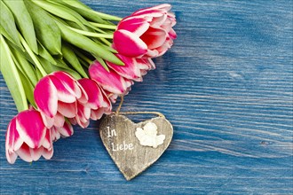 Bouquet of tulips on blue background and wooden heart