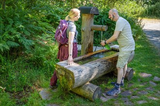 Hiking couple filling drinking bottle at the wooden fountain on the hiking trail Sprollenhaeuser Hut