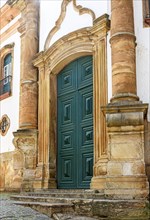 Portal of a historic baroque church in the city of Ouro Preto in wood framed by a stone arch.