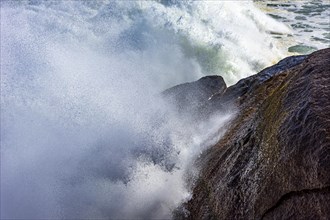 Big wave crashing against the rocks with sea water splashing in the air during storm