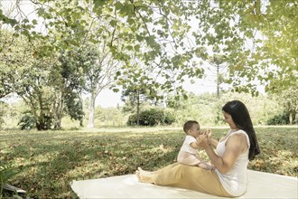Mother and her baby daughter sitting on a blanket in a park on a sunny day. The image promotes the idea of motherhood as a joyful and fulfilling experience