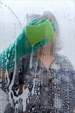 Closeup of a woman cleaning the windows of her house with a green rag and rubber gloves