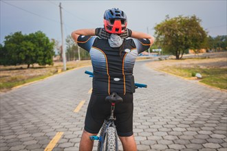 Rear view of a cyclist with neck pain with the bike. Back view of a cyclist man having neck pain while riding a bike