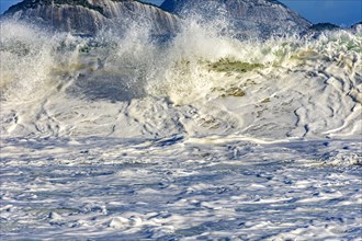 Beautiful and strong sea wave on the beach with water drops and foam splashing in the air on a sunny day