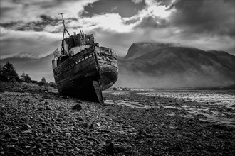 Stranded fishing boat and Ben Nevis from the shore of Loch Linnhe in black and white