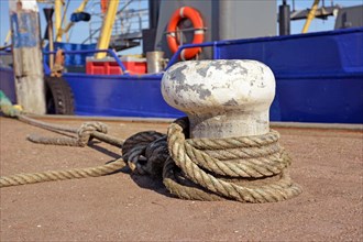 Bollard with robe attached to it to secure anchored boat in Oudeschild harbor on island Texel in North Netherlands