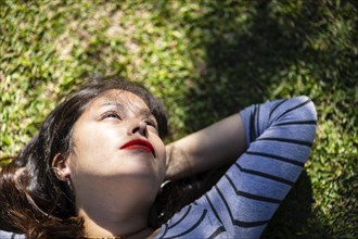 Overhead portrait of an andean woman lying on the grass with lights and shadows filtered by the tree branches