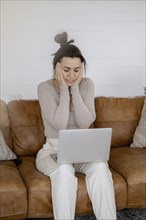 Woman sits on couch with laptop completely overwhelmed