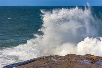 Wave breaking over rocks with water splashing with blue sky on a rough sea day in Rio de Janeiro