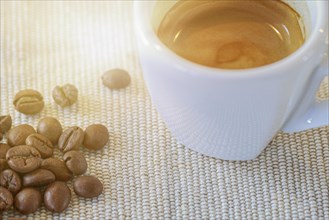 A filled espresso cup stands next to coffee beans on a table