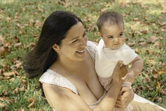 Pretty latin mother with baby in arms enjoying outdoors together. The image portrays the beauty and naturalness of the bond between a mother and her baby