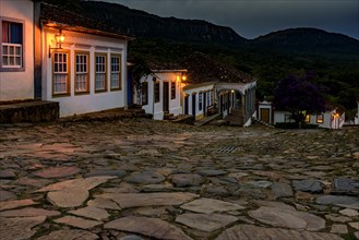 Streets and houses of the historic city of Tiradentes illuminated at dusk with the mountains in the background