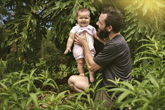 A happy family. Dad and baby play and laugh on a walk. A baby girl looks at the camera smiling