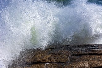 Strong wave crashing against the rocks with sea water and foam splashing in the air