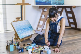 Woman artist painting on a canvas a blue abstract painting. Creative ywoman working on the floor in her art studio