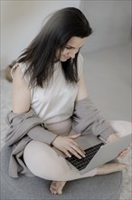 Young woman sitting comfortably with laptop on a stool in the living room