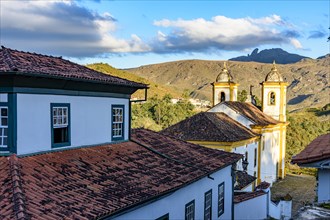 Historic church tower in baroque architecture and old colonial houses with the mountains in the background in Ouro Preto