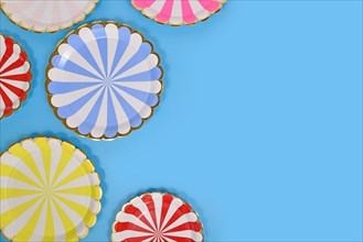 Colorful striped paper party plates on side of blue background with copy space
