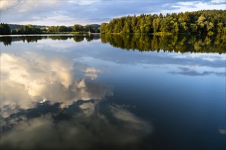 The Postfelden reservoir in the evening at golden hour. Dramatic clouds are reflected in the calm water. Hoellbachtal